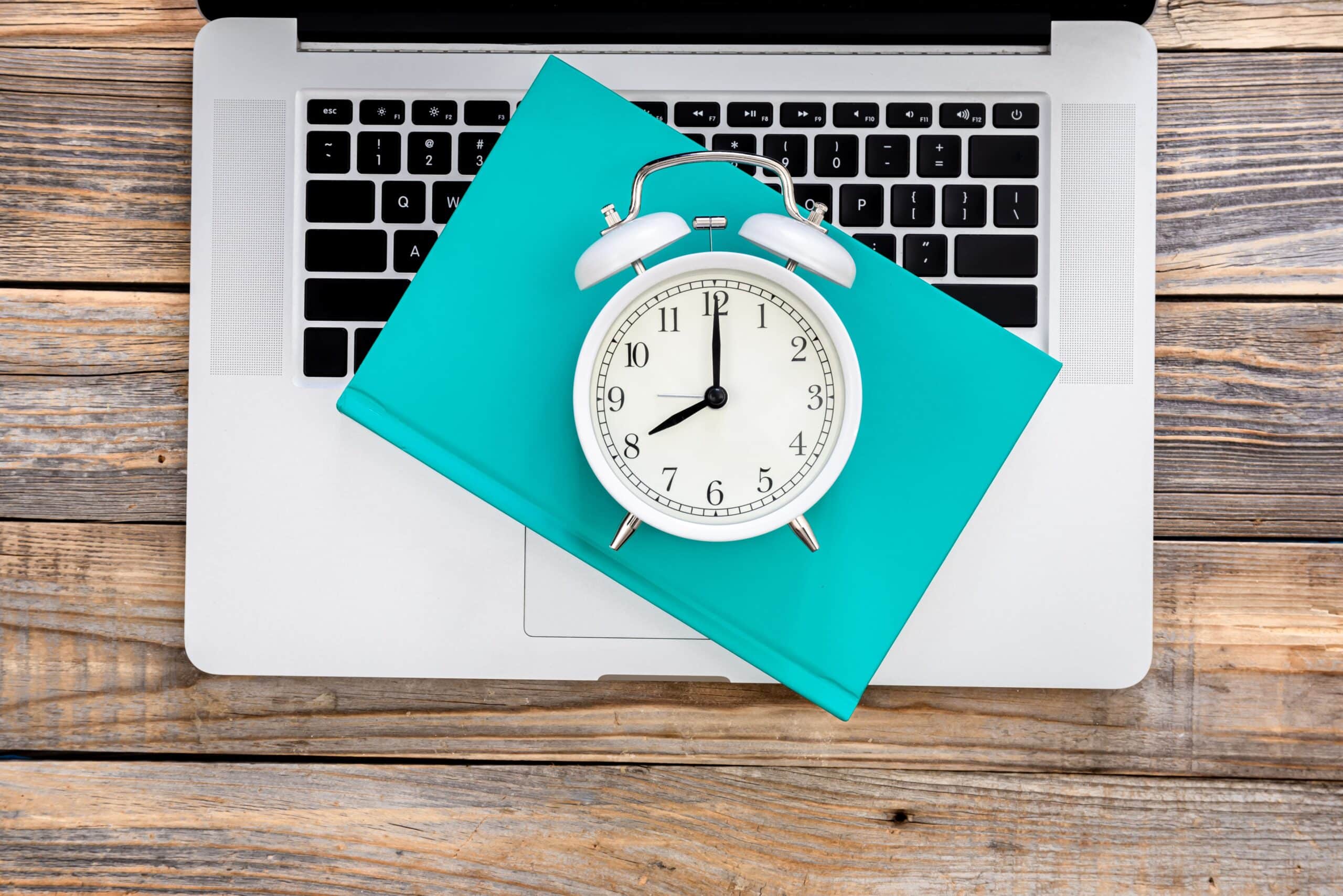 Ordenador portátil y un reloj simulando un software de control horario para el registro digital de la jornada laboral de los empleados.